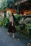 Woman wearing Wildalaya Everyday Hemp Wrap Skirt full-length front view, adjustable tie, natural colour walking on a sidewalk with plants and a building in the background