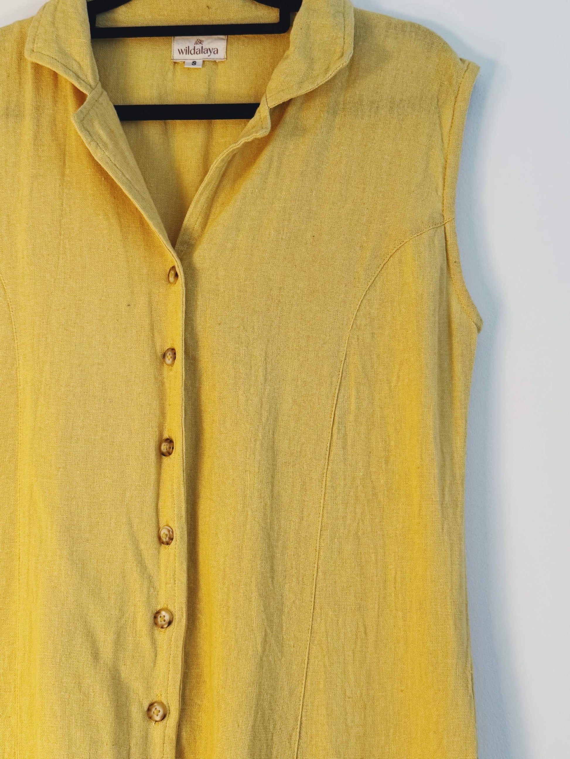 Yellow hemp sleeveless shirt dress on a hanger with a visible brand label against a light gray background