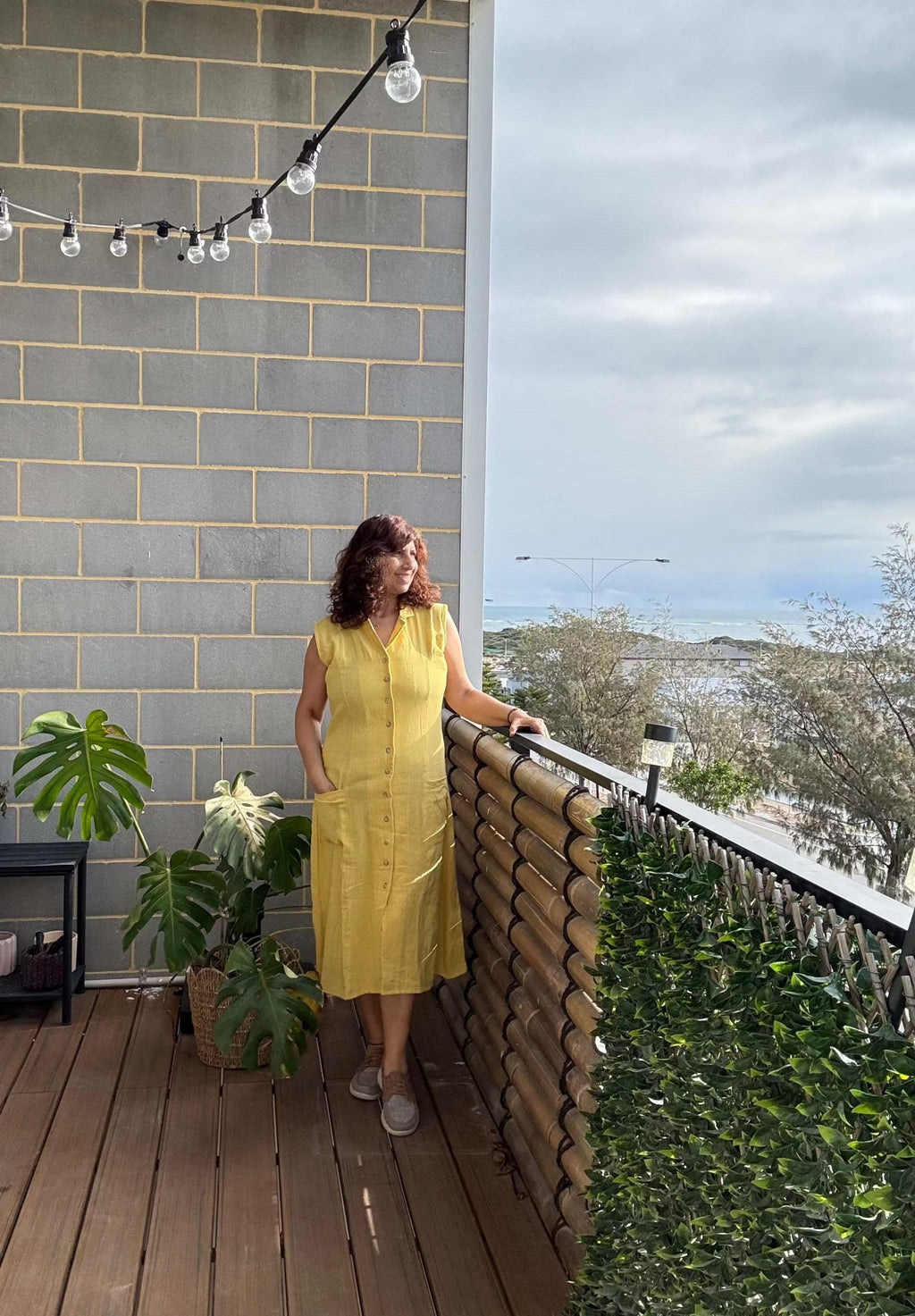 Woman in a Hemp yellow dress standing on a balcony with a scenic view.