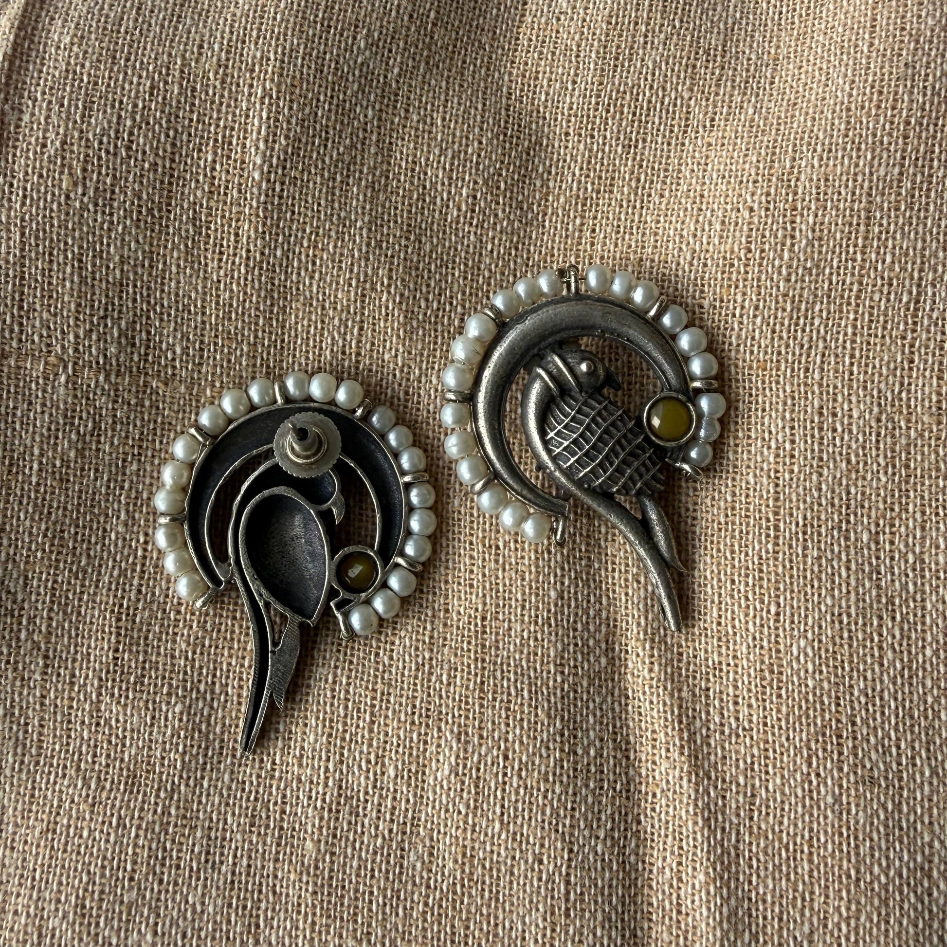 Pair of silver earrings with pearl accents on a beige fabric background
