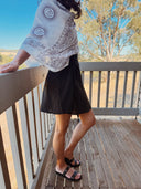 Model wearing a white patterned top and black hemp little skirt on a wooden deck with trees in the background