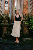 Woman in black top and Sandy Wrap Wildalaya skirt standing in front of a traditional architectural structure with lush greenery.