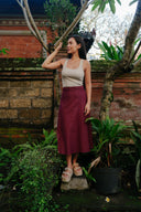 Woman wearing Wildalaya Wrap Skirt mulberry standing outdoors in a garden with plants and a brick wall in the background