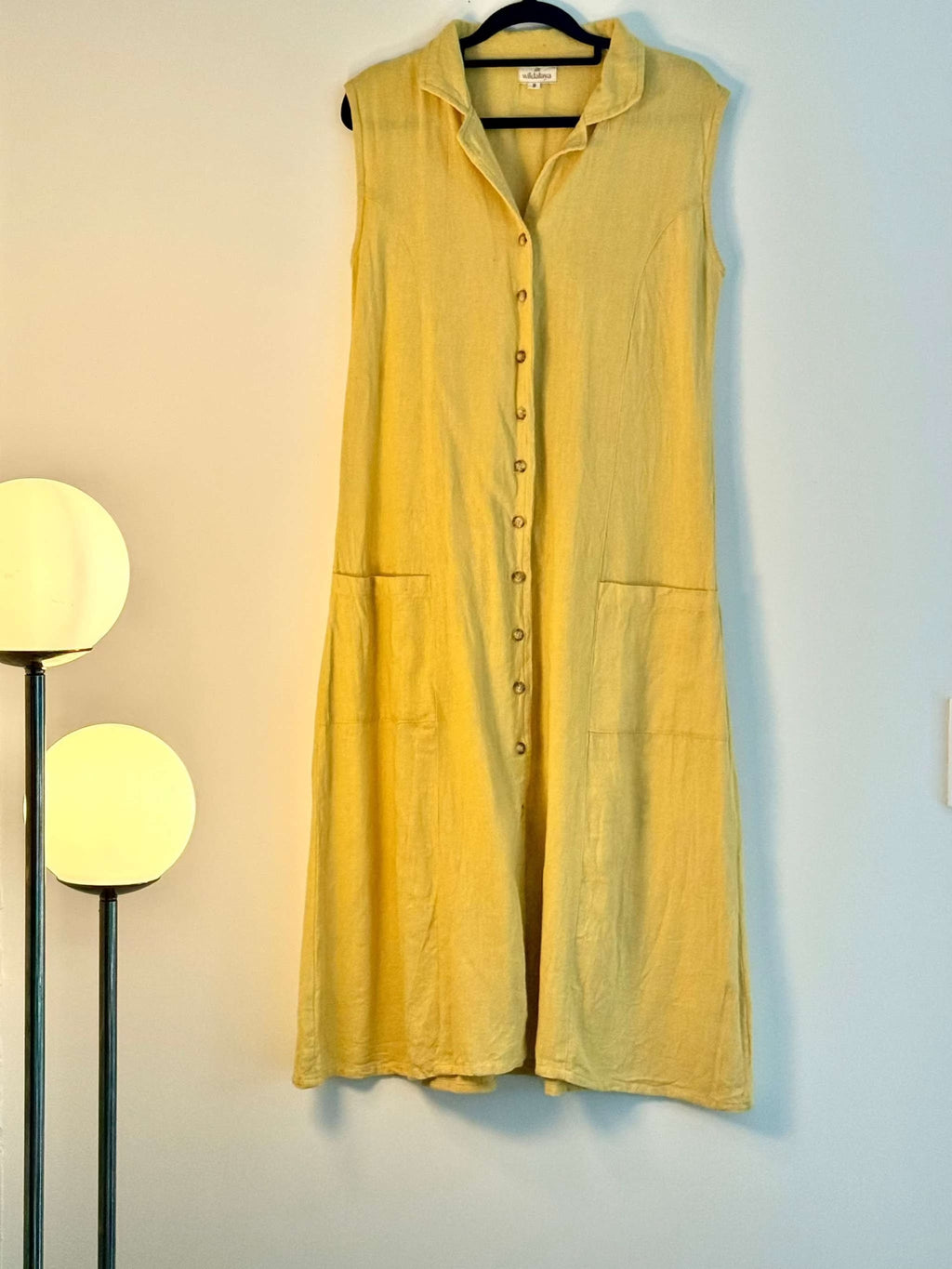 Yellow sleeveless dress hanging on a hanger against a light wall.